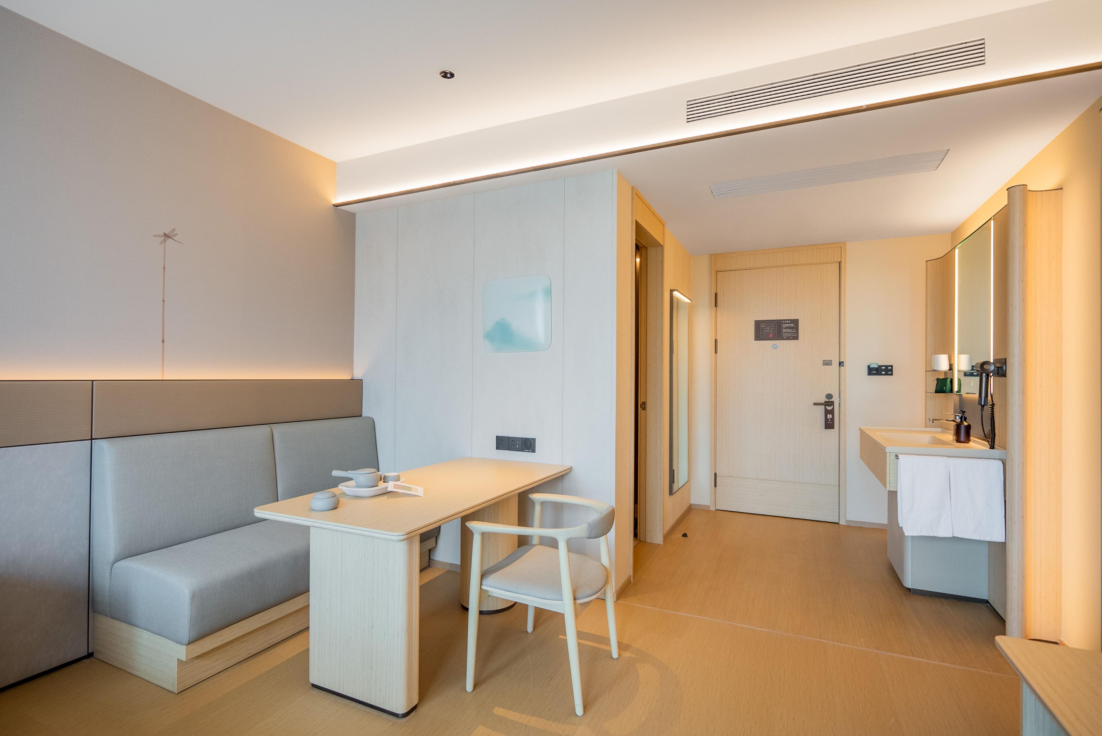 Una habitación de hotel moderna con sofá, escritorio, silla, espejo y baño.