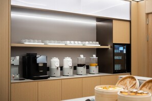 Un área de cocina moderna con cafetera, dispensadores de leche y un refrigerador.