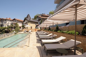 A poolside area with lounge chairs and umbrellas, a clear pool, and buildings in the background. - Eurostars Villa Itziar (San Sebastián)