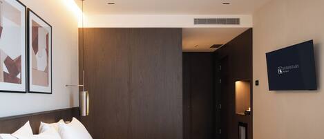 A hotel room with a bed, a wall-mounted TV, and a door leading to another room.