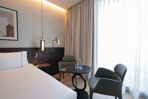 Habitación de hotel con una cama, dos sillas, una mesita, una lámpara y un cuadro en la pared.