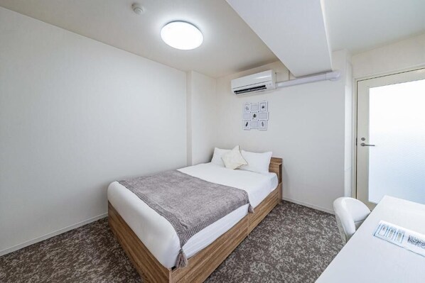 A bedroom with a bed, a desk, an air conditioning unit, and a door. - Hoshi noYado Imamiya (Osaka)