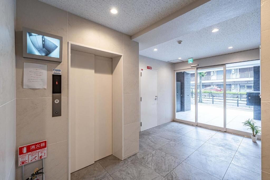 A hotel lobby with a reception desk, a fire extinguisher, an elevator, and a glass door leading outside.