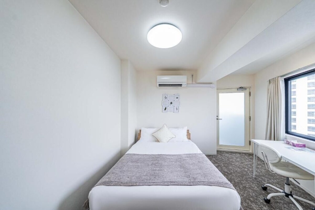 A hotel room with a bed, a desk, an air conditioning unit, and a window.