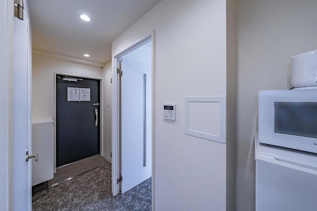 A hallway with a closed door, a thermostat, and a microwave.