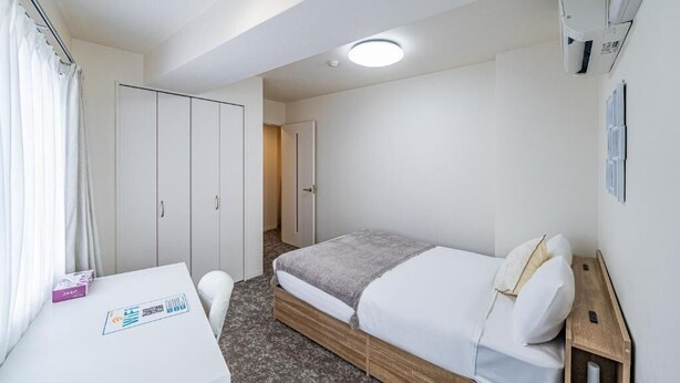 Ett hotellrum med en säng, ett skrivbord, en stol, en garderob och en dörr till badrummet.