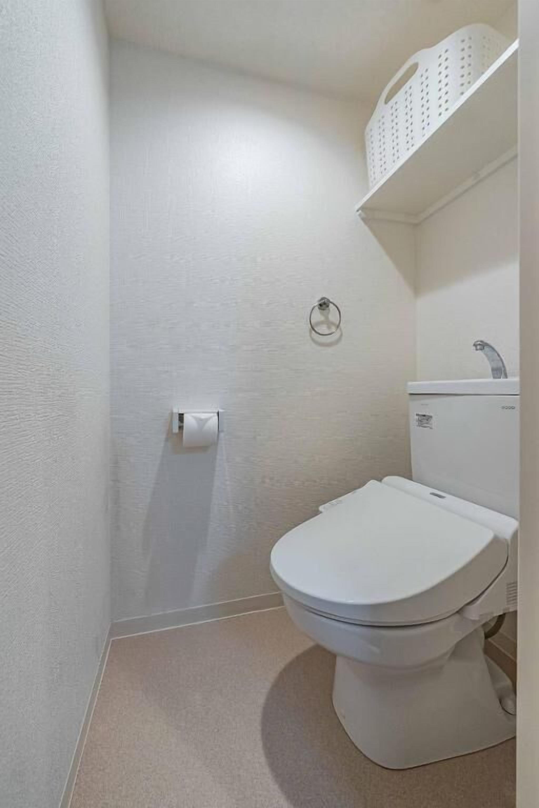 Une petite salle de bain blanche, avec des toilettes, un lavabo et un panier fixé au mur.