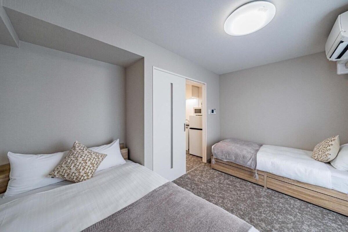 A hotel room with two beds, a small kitchenette, and a ceiling light.