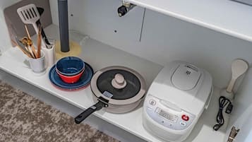 A kitchen with a rice cooker, a pot, a bowl, and utensils on a shelf.