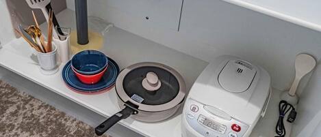 Een keuken met een rijstkoker, pan, kom en keukengerei op een plank.