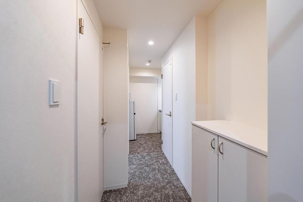 A narrow hallway with white walls, a carpeted floor, and a door at the end.