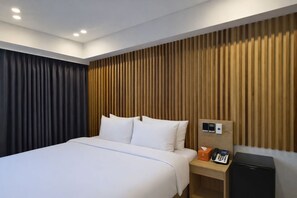 Een hotelkamer met een bed, een houten hoofdbord, een nachtkastje met een telefoon en een klein apparaat, en een donker gordijn.