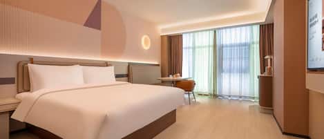 A hotel room with a large bed, a desk, and a chair. There is a large window with curtains.
