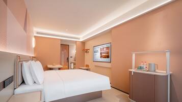A hotel room with a bed, bedside table, and a small table with a chair. There is a wall-mounted TV and a mirror above the table.