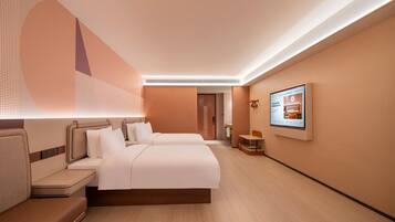 A hotel room with two beds, a seating area, a TV, and a bathroom visible in the background.