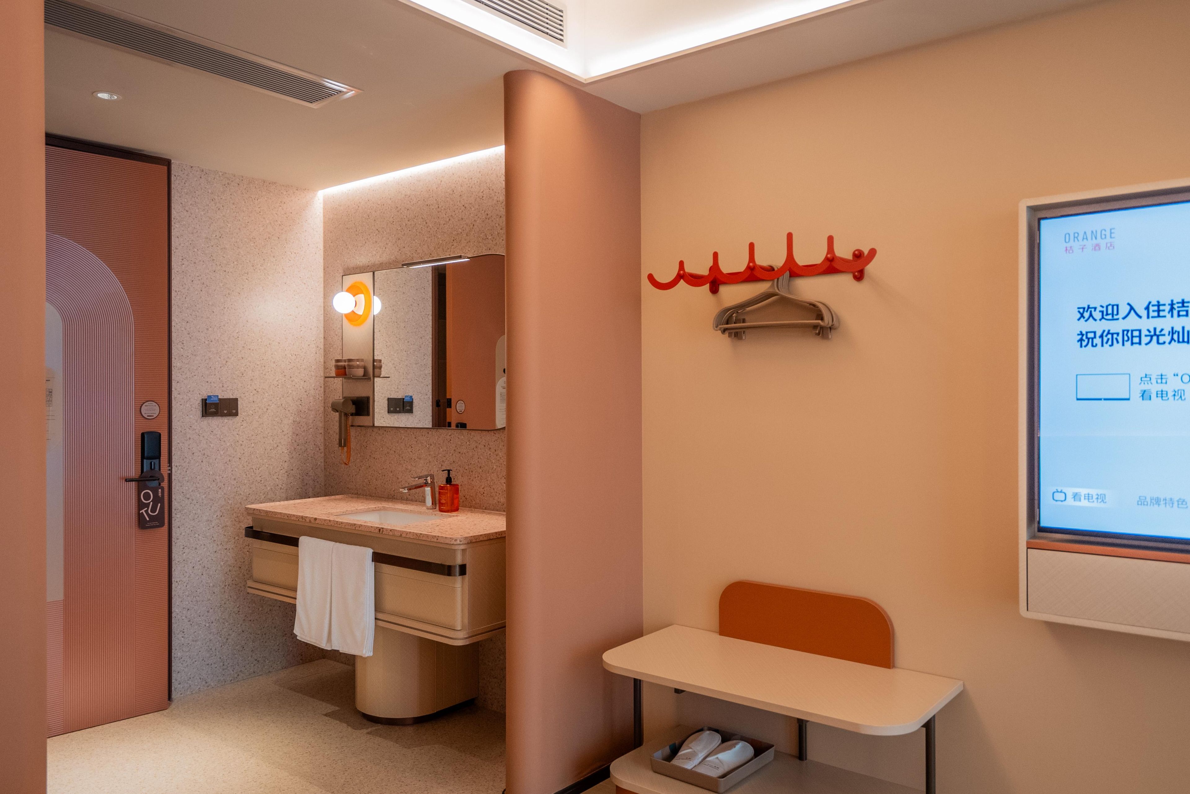 A hotel bathroom with a sink, mirror, towel rack, and a small table with shoes.