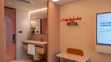 A hotel bathroom with a sink, mirror, towel rack, and a small table with shoes.