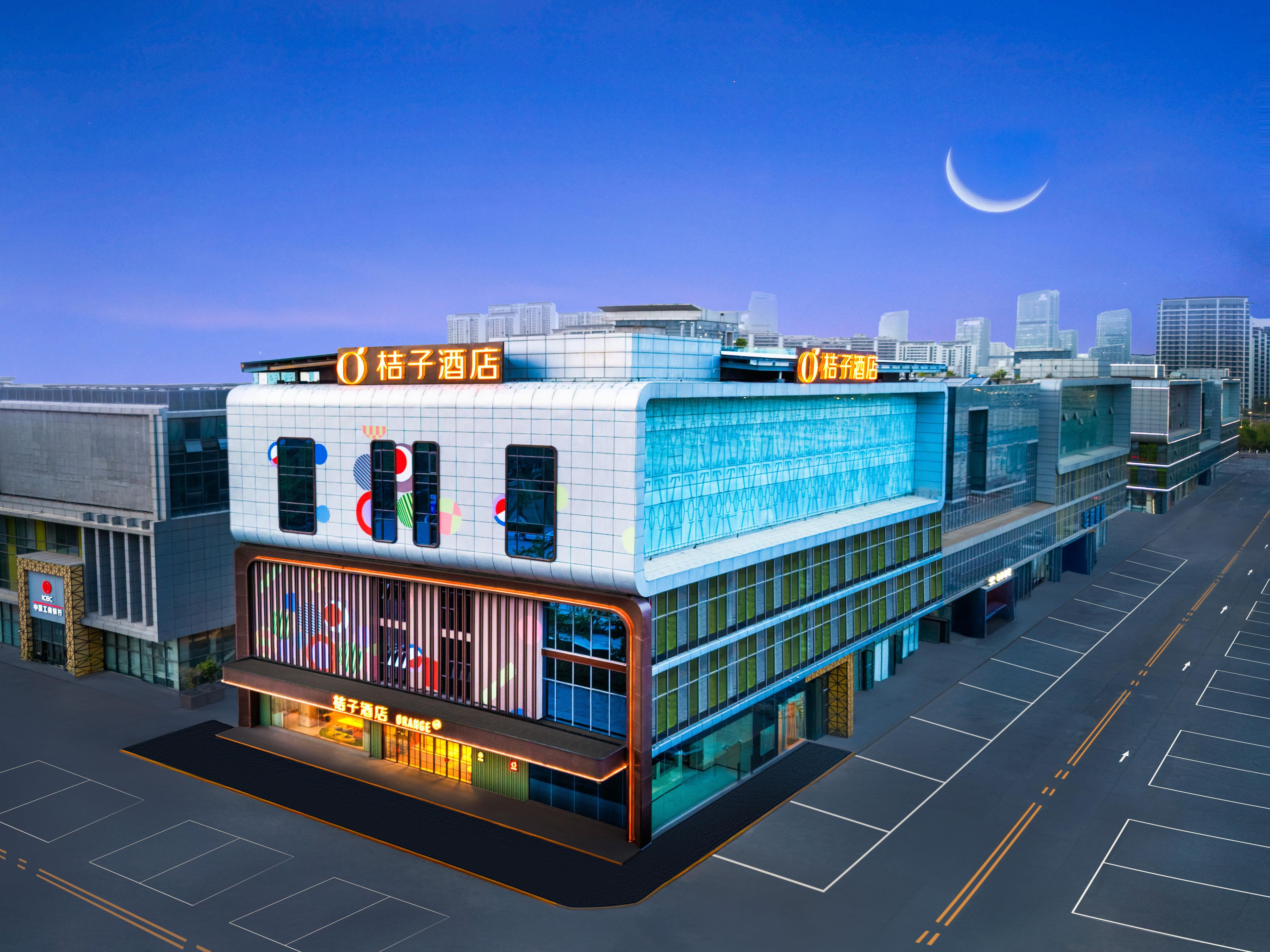 A modern hotel with a prominent sign, large windows, and a parking lot.