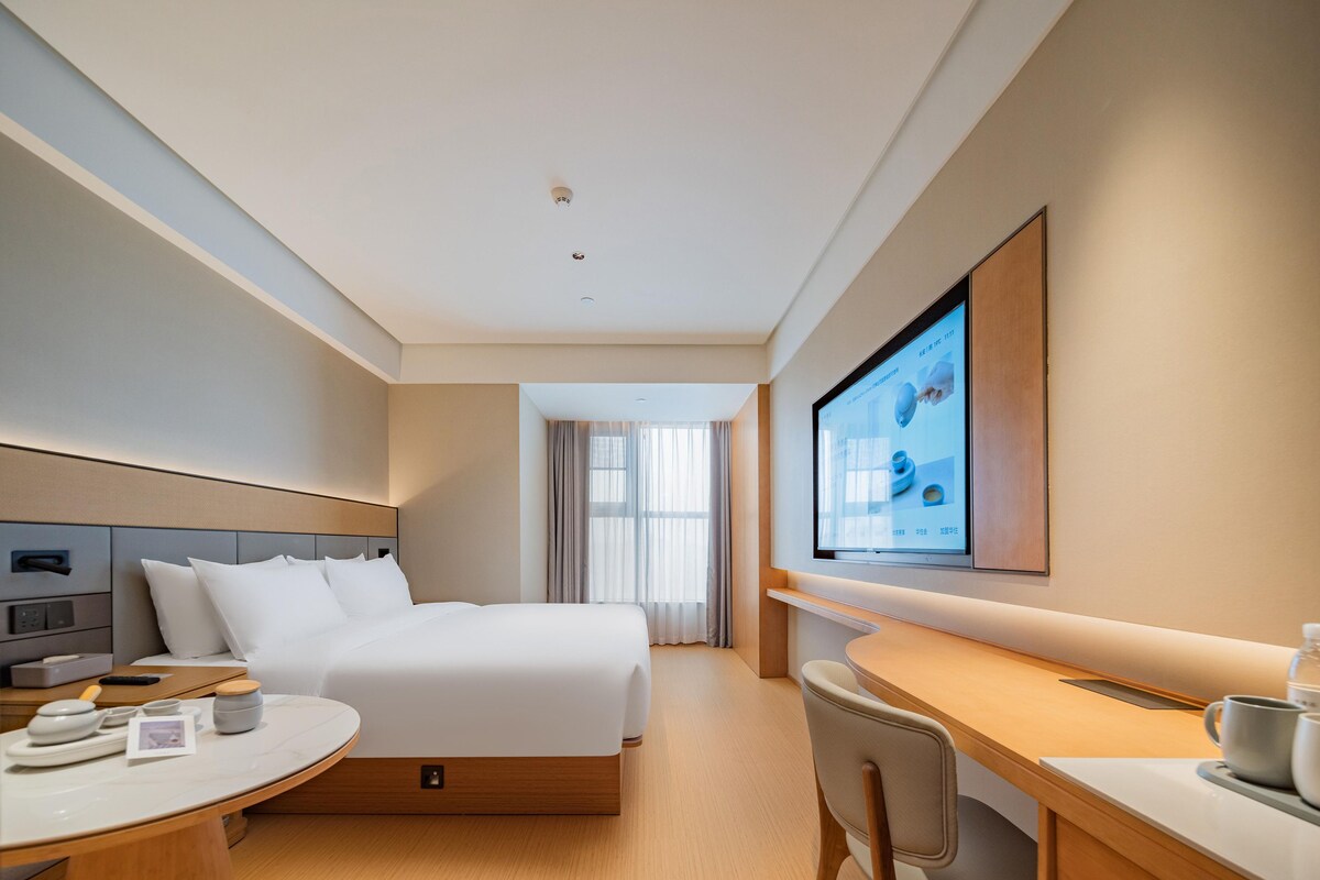 A hotel room with a bed, a desk, a chair, a television, and a window.