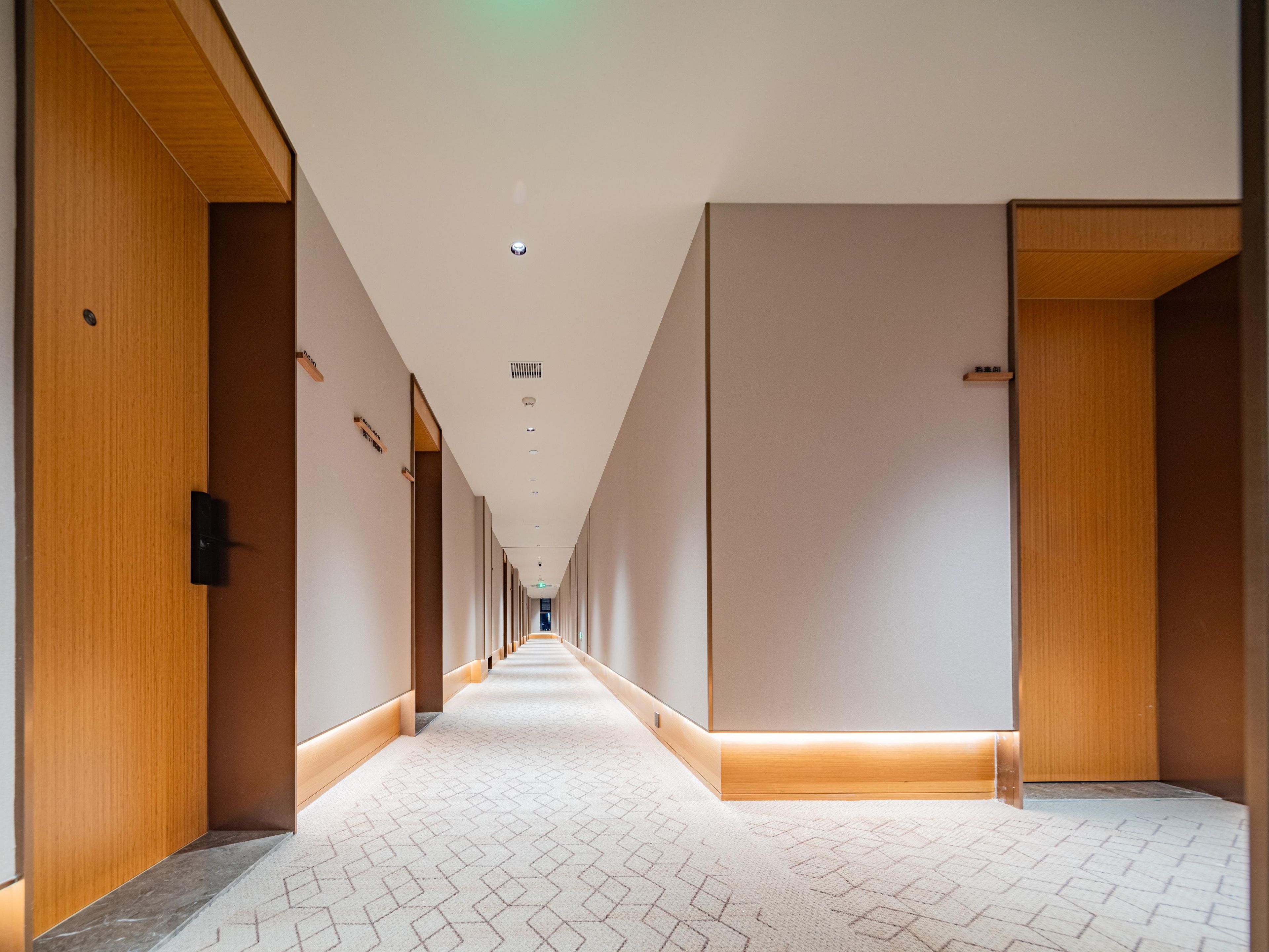 A long, narrow hotel corridor with wooden doors on either side and a patterned carpet.