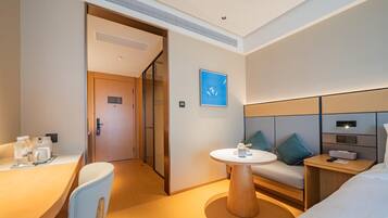 A hotel room with a bed, a desk, a chair, a round table, and a sofa.