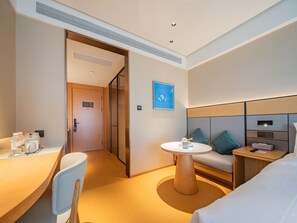 A hotel room with a bed, a desk, a chair, a round table, and a sofa.