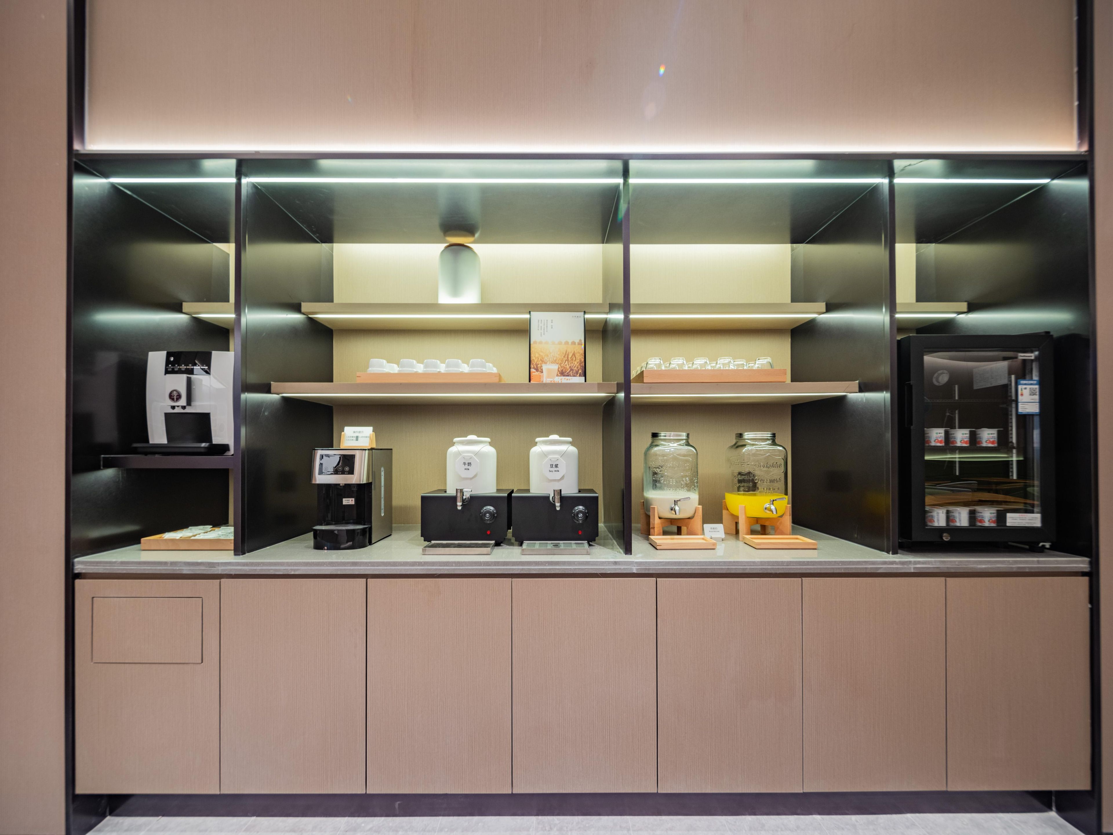 A coffee station with multiple dispensers and a refrigerator.
