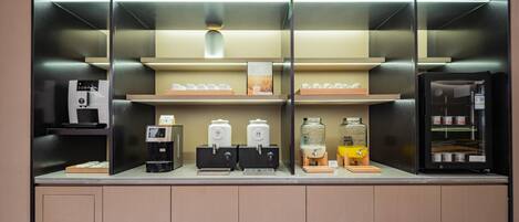 A coffee station with multiple dispensers and a refrigerator.