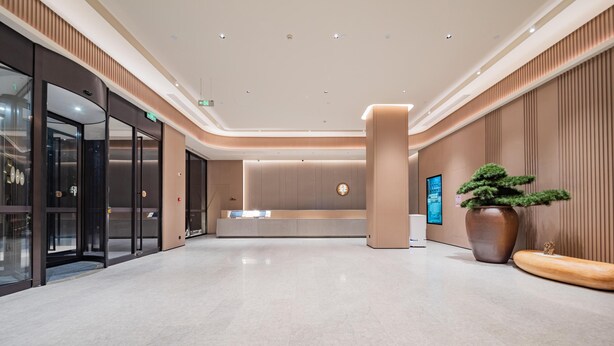 Un moderno vestíbulo de hotel con una recepción, una pantalla informativa digital y una planta en maceta grande.