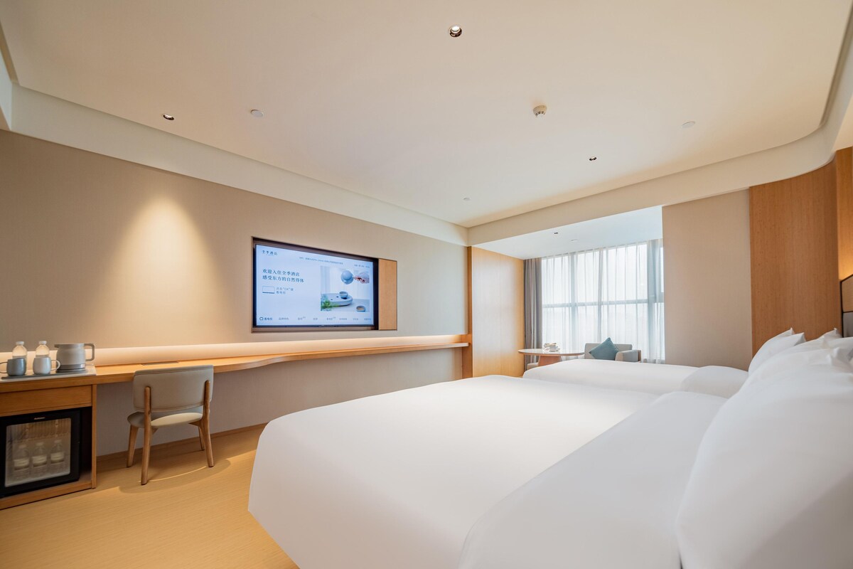 A hotel room with a large bed, a desk with a computer, and a television mounted on the wall.