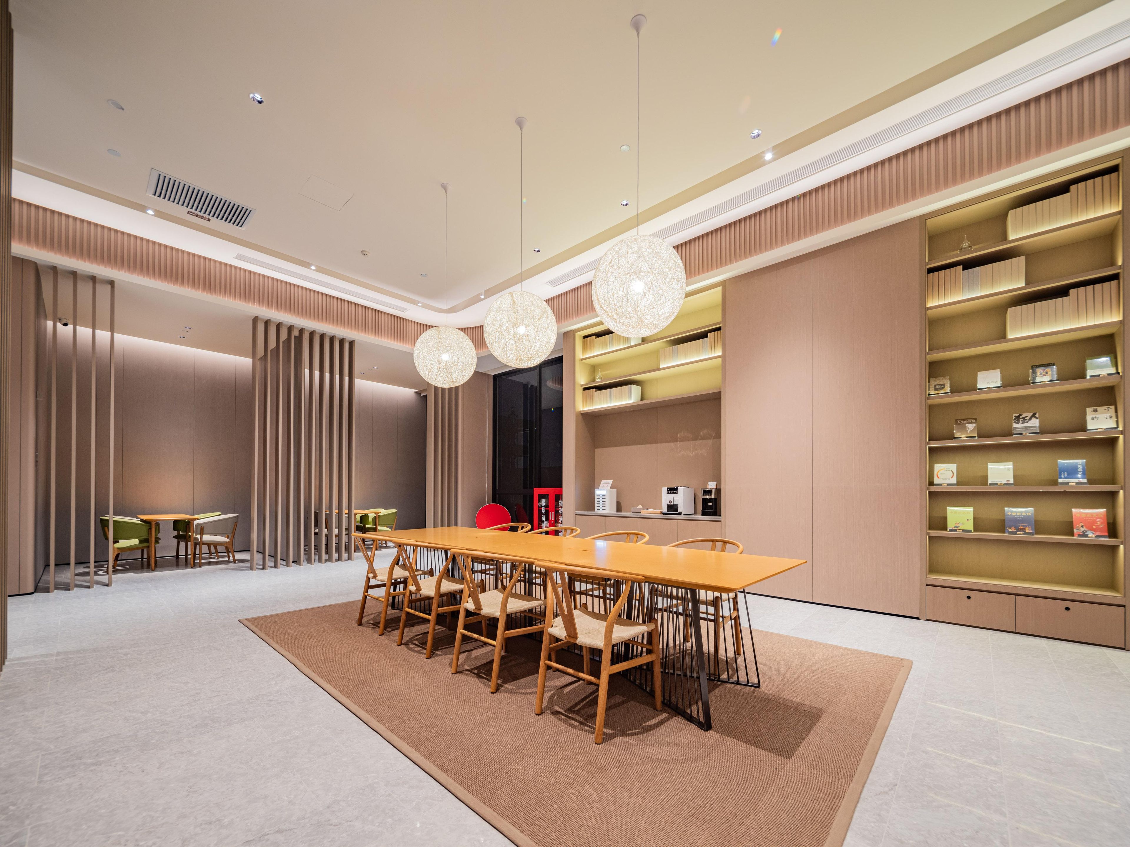 Una habitación de hotel moderna con zona de comedor que incluye una mesa y sillas de madera, una lámpara de araña grande y estanterías empotradas.