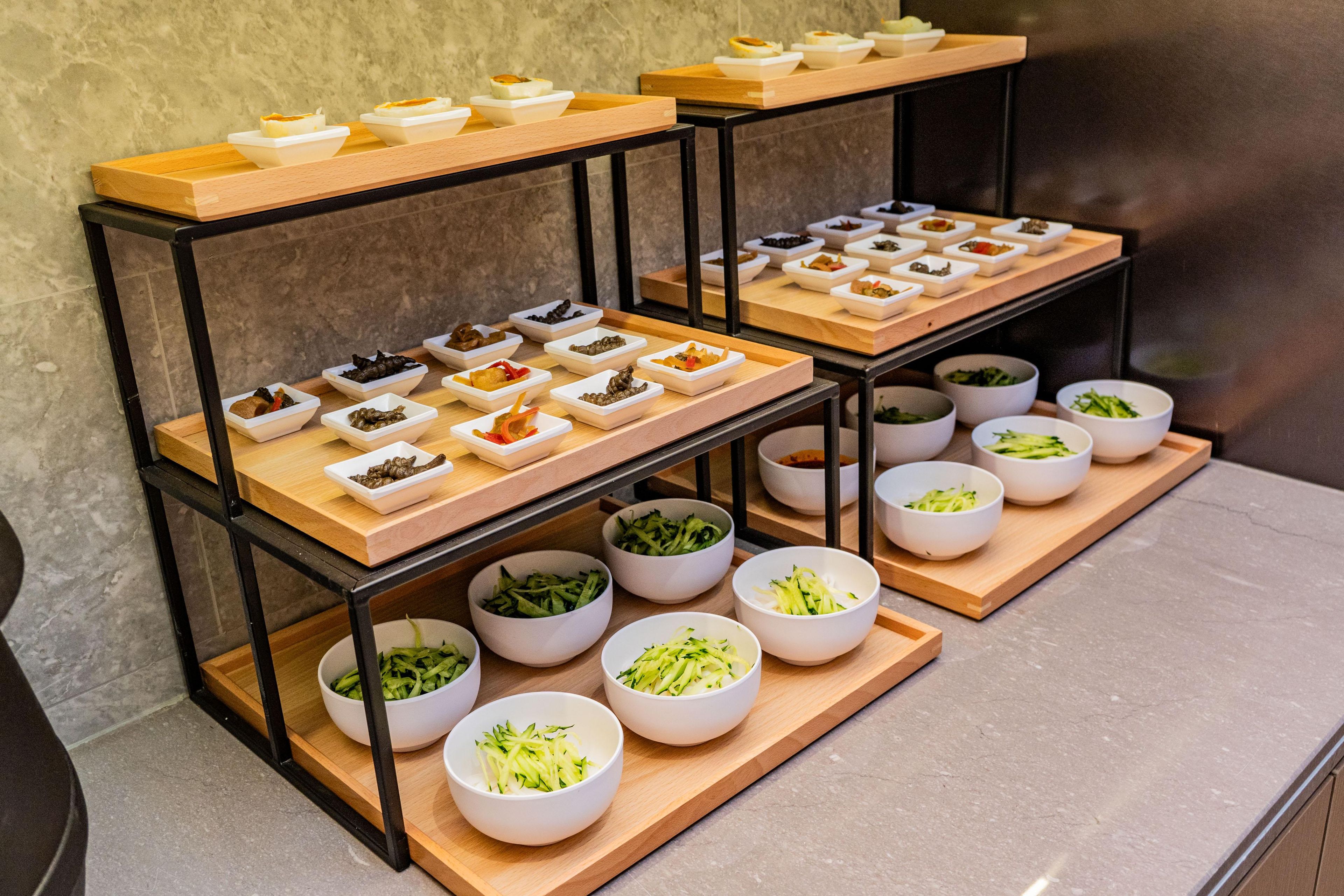 A buffet setup with various food items arranged on wooden boards and white bowls.