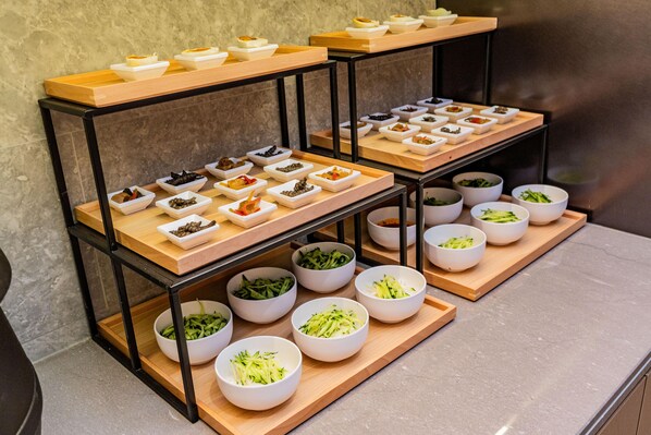 A buffet setup with various food items arranged on wooden boards and white bowls.