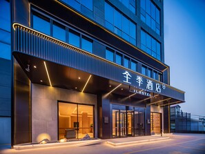 A modern hotel entrance with a glass facade, illuminated signage, and a welcoming outdoor area.