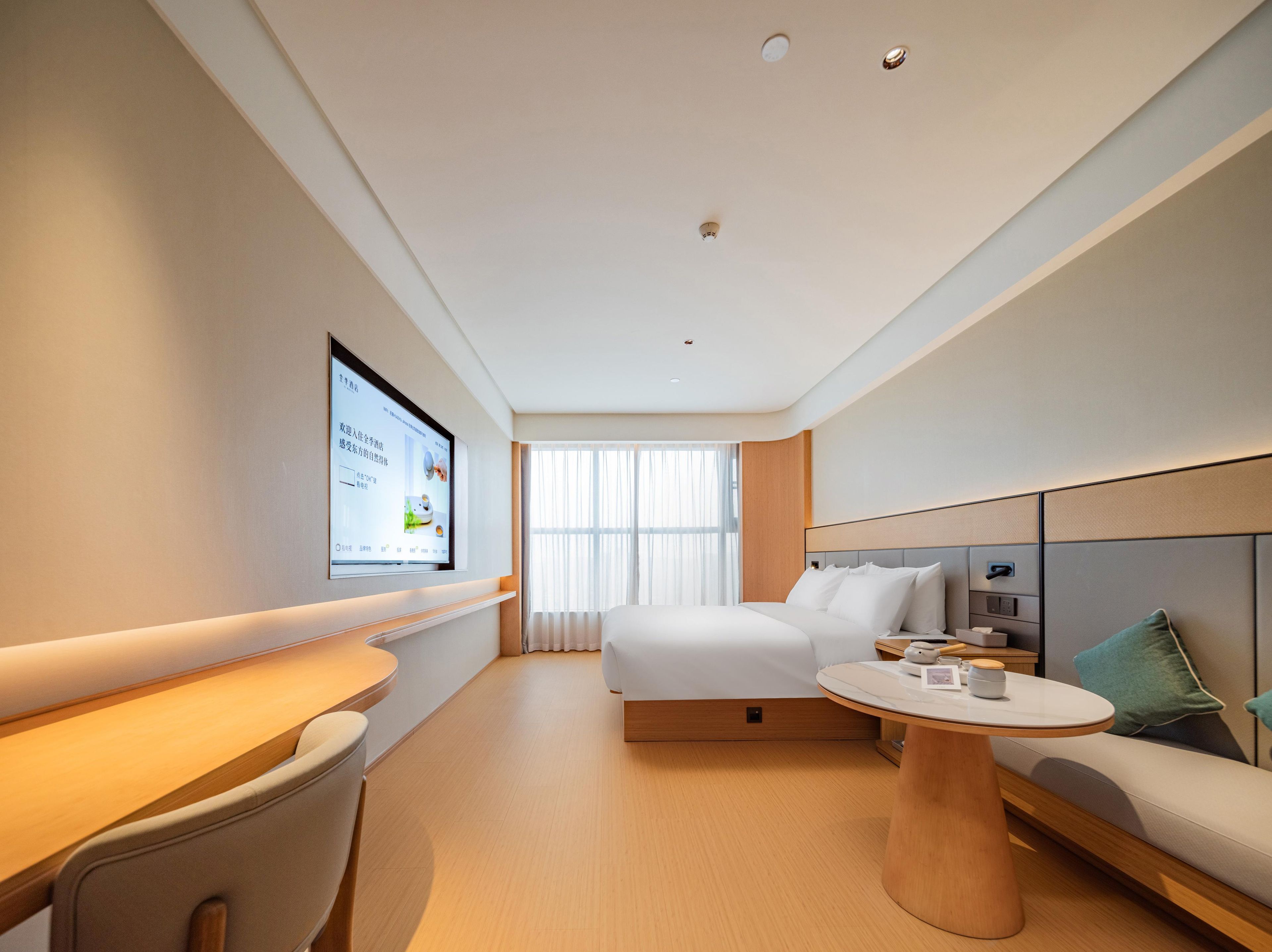 Een moderne hotelkamer met een bed, een bureau, een ronde tafel en een aan de muur bevestigde televisie.