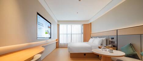 A modern hotel room with a bed, a desk, a round table, and a TV mounted on the wall.