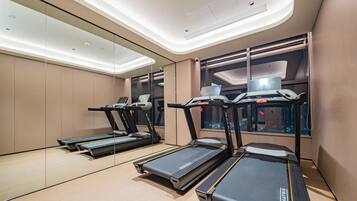 A modern gym with treadmills, a mirrored wall, and a window with a laptop on the desk.