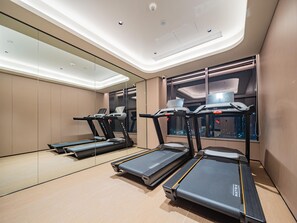 A modern gym with treadmills, a mirrored wall, and a window with a laptop on the desk.