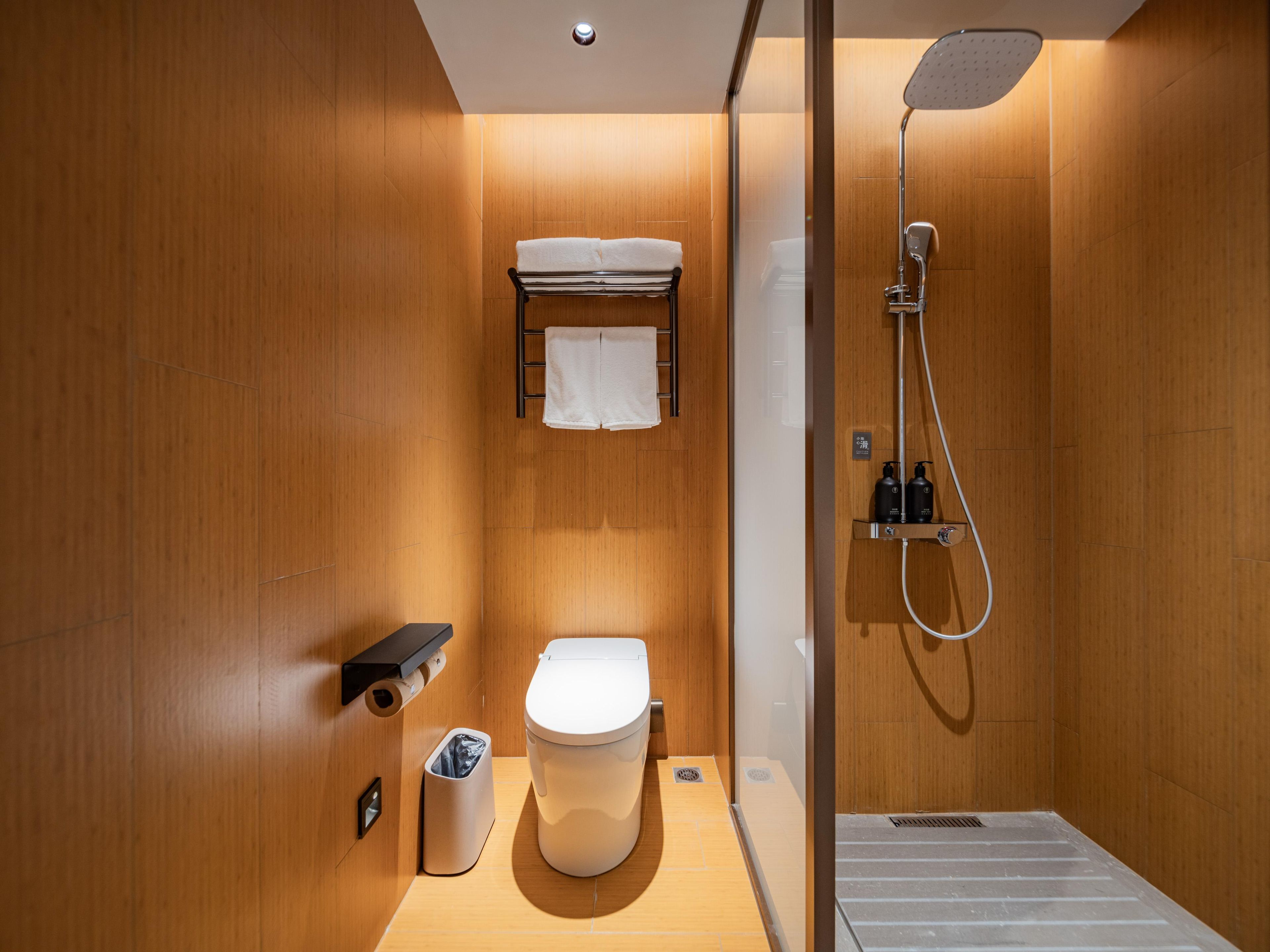Ein modernes Badezimmer mit einer Holzvertäfelung, einer weißen Toilette, einem Handtuchhalter, einer Dusche und einem Mülleimer.