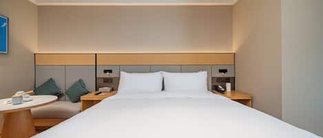 A hotel room with a large bed, bedside tables, a round table, and a wall-mounted control panel.