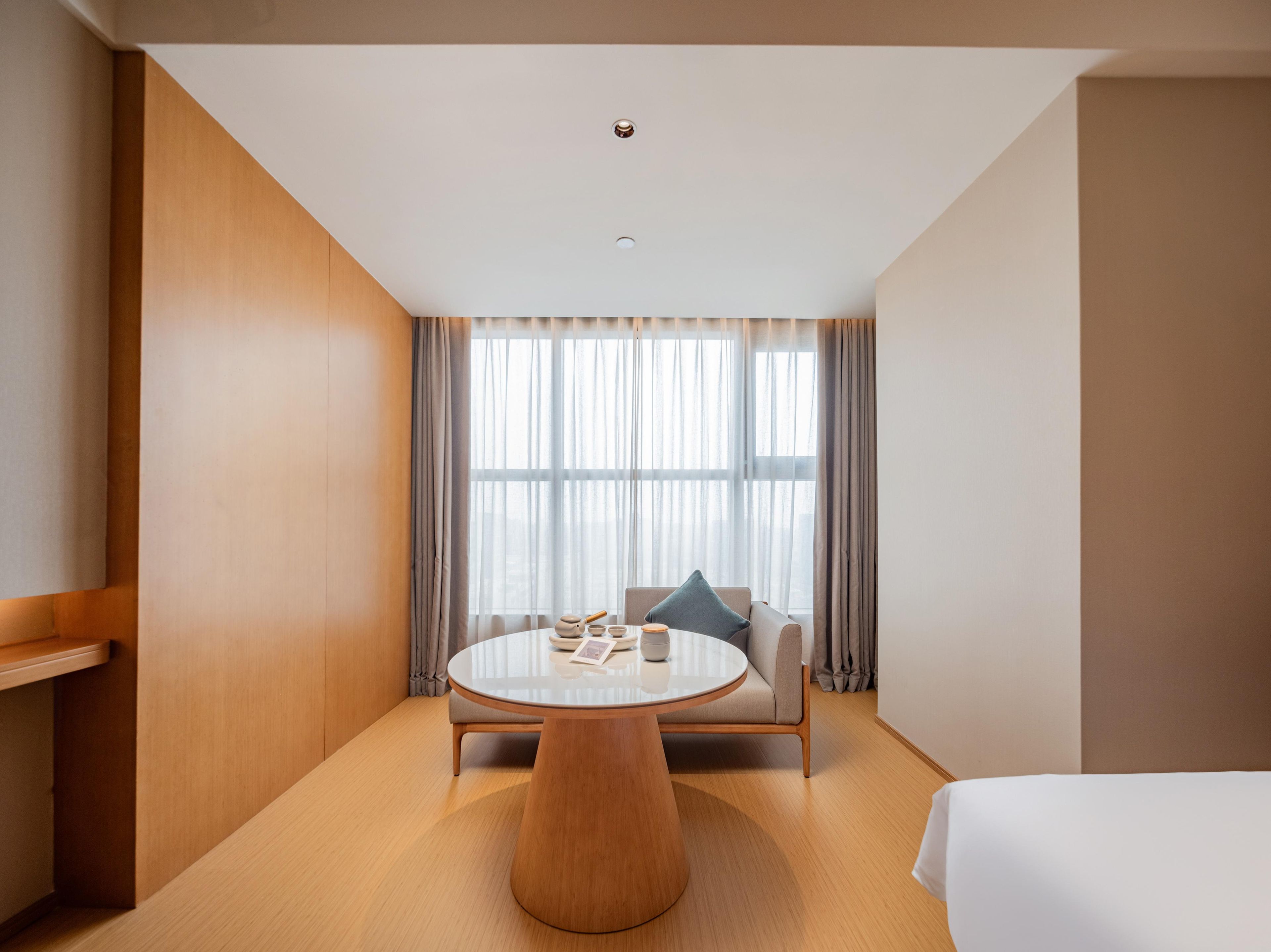 A hotel room with a round table, a sofa, a bed, and a large window with curtains.