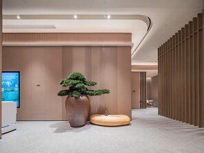 A modern interior with a large potted bonsai tree, a wooden stool, and a digital screen on the wall. - JI Hotel Xian National Supercomputing Center East (Xi'an)