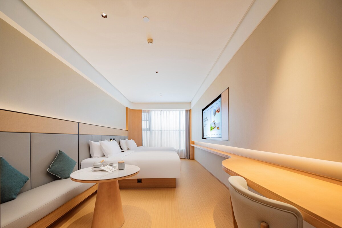 A modern hotel room with a bed, a sofa, a desk, and a television mounted on the wall.