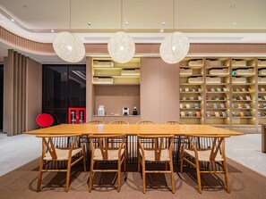 A modern dining area with a long wooden table and chairs, surrounded by bookshelves with books. - JI Hotel Xian National Supercomputing Center East (Xi'an)