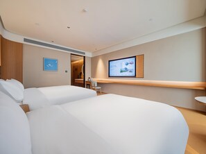 Habitación de hotel con dos camas, un escritorio, una silla, un televisor montado en la pared y una puerta que da al baño.