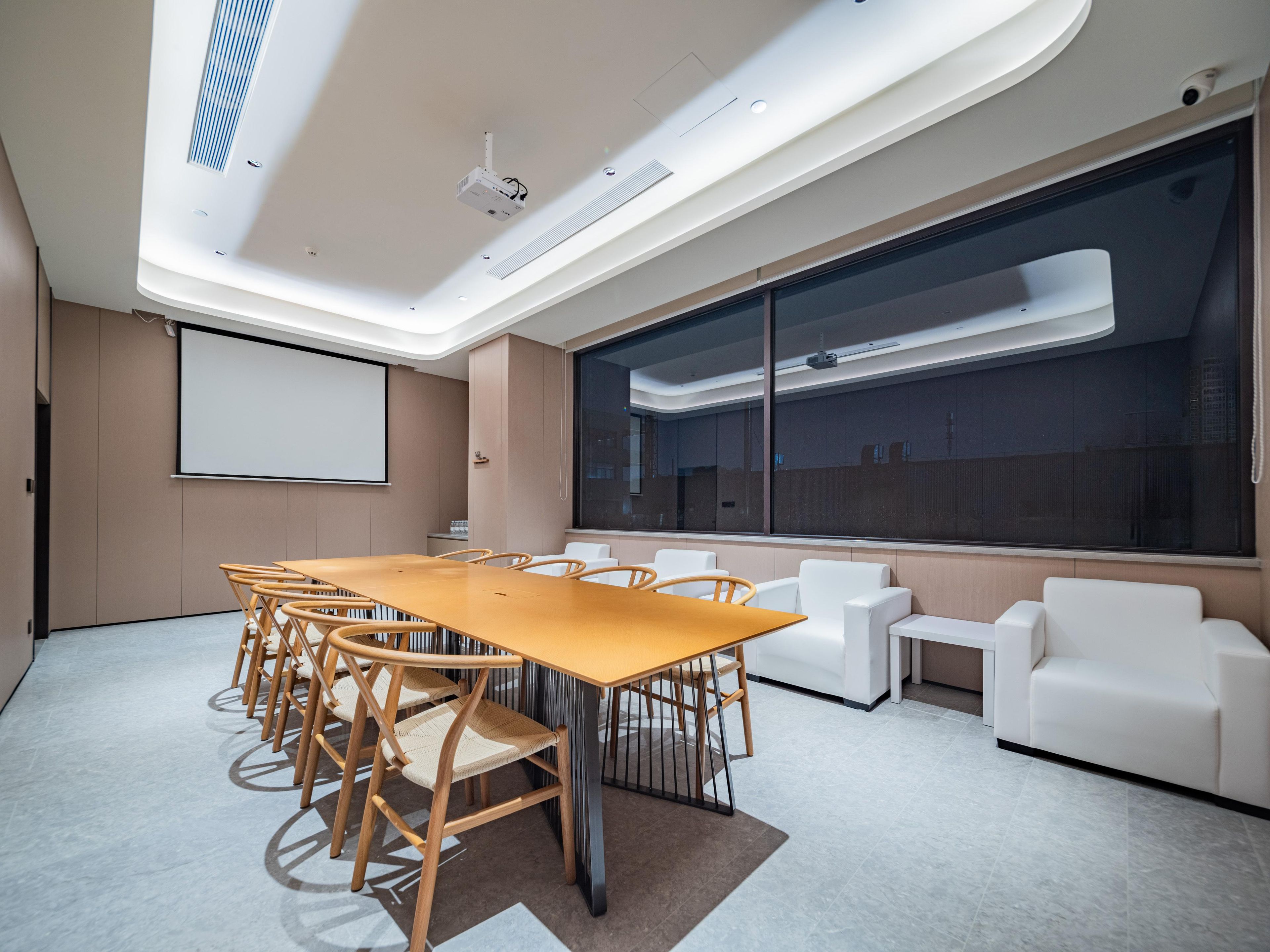 A conference room with a long table, chairs, a projector screen, and a large window.