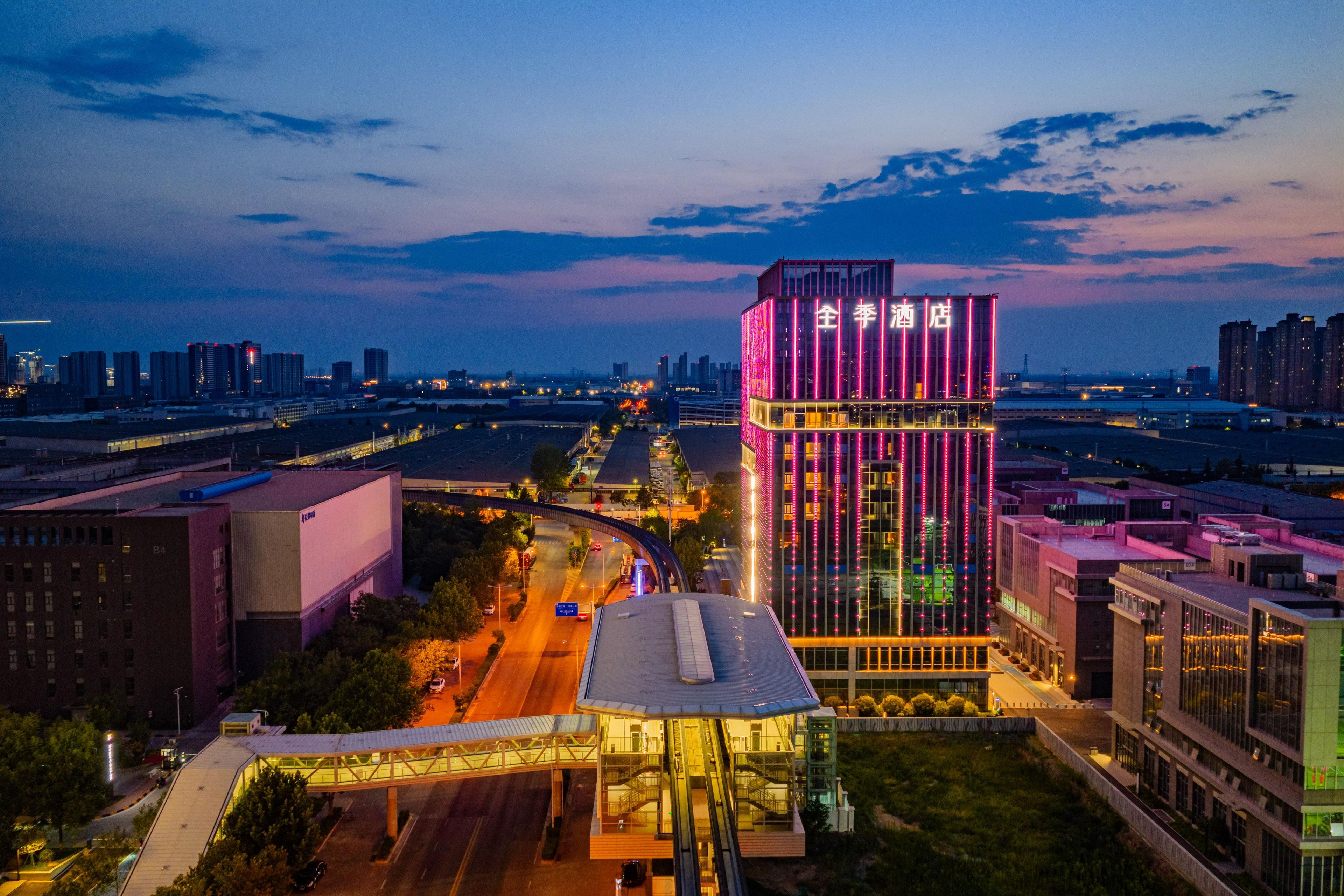 A modern hotel with a prominent tower featuring vertical neon lights, surrounded by urban infrastructure.