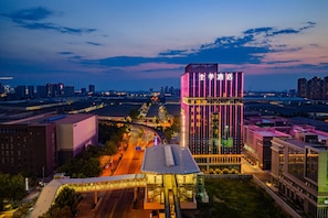 A modern hotel with a prominent tower featuring vertical neon lights, surrounded by urban infrastructure. - JI Hotel (Xi'an)