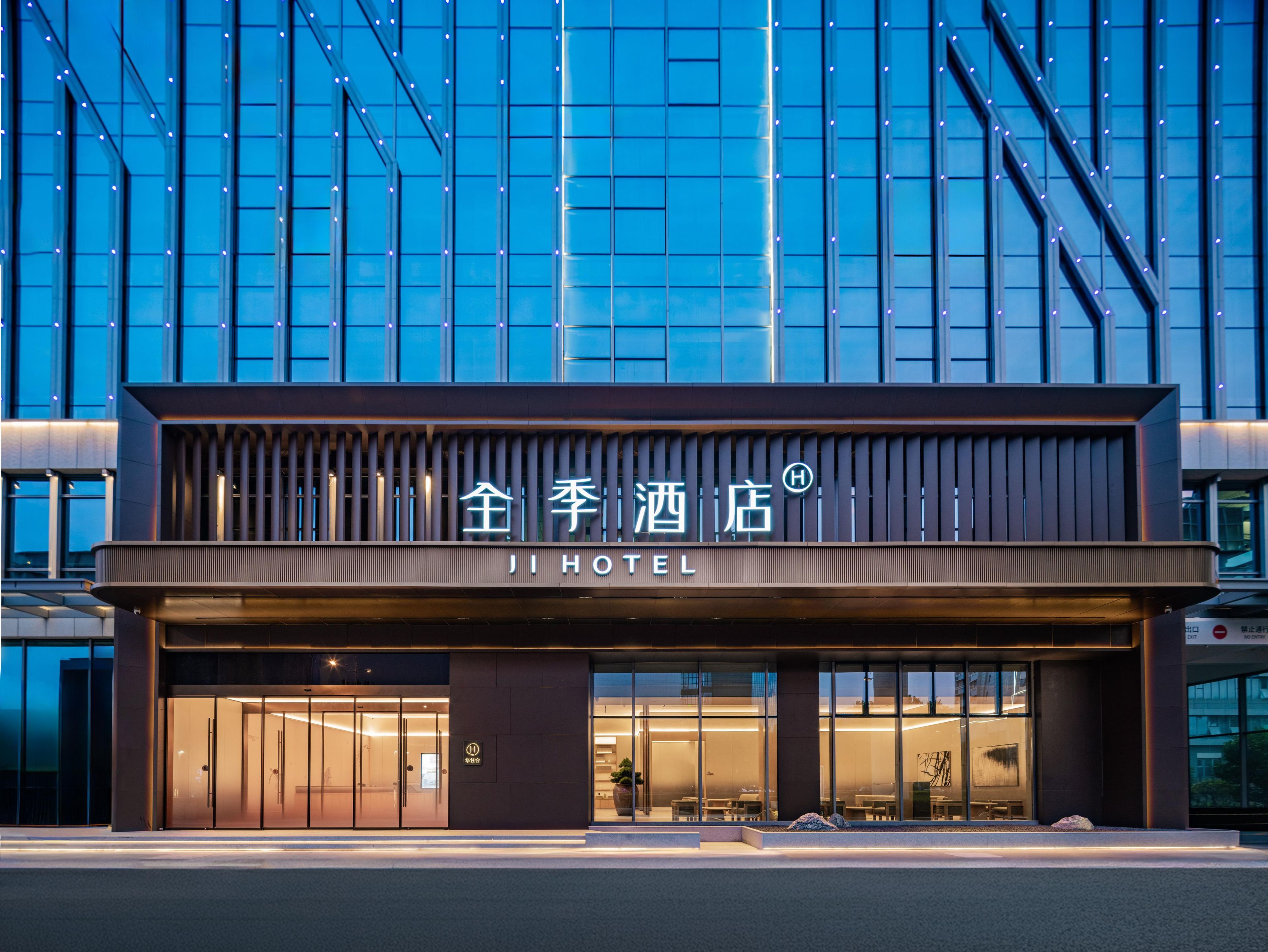 A modern hotel facade with a prominent entrance, large windows, and a sign indicating the name 'JI HOTEL'.