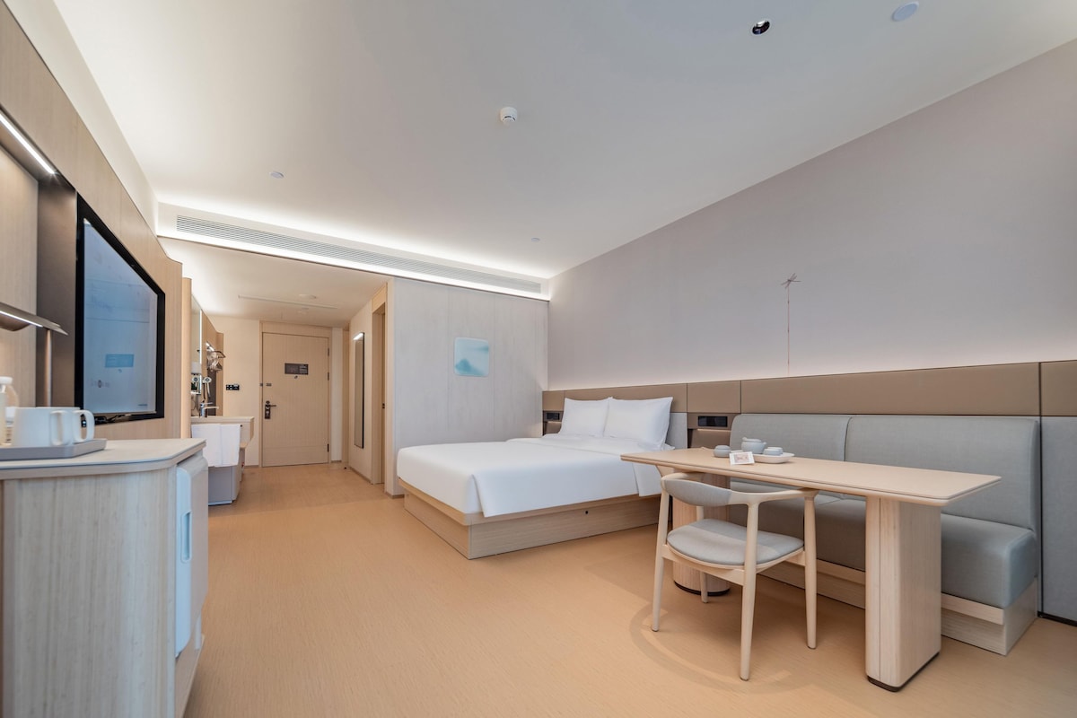 A modern hotel room with a bed, a desk, and a seating area.